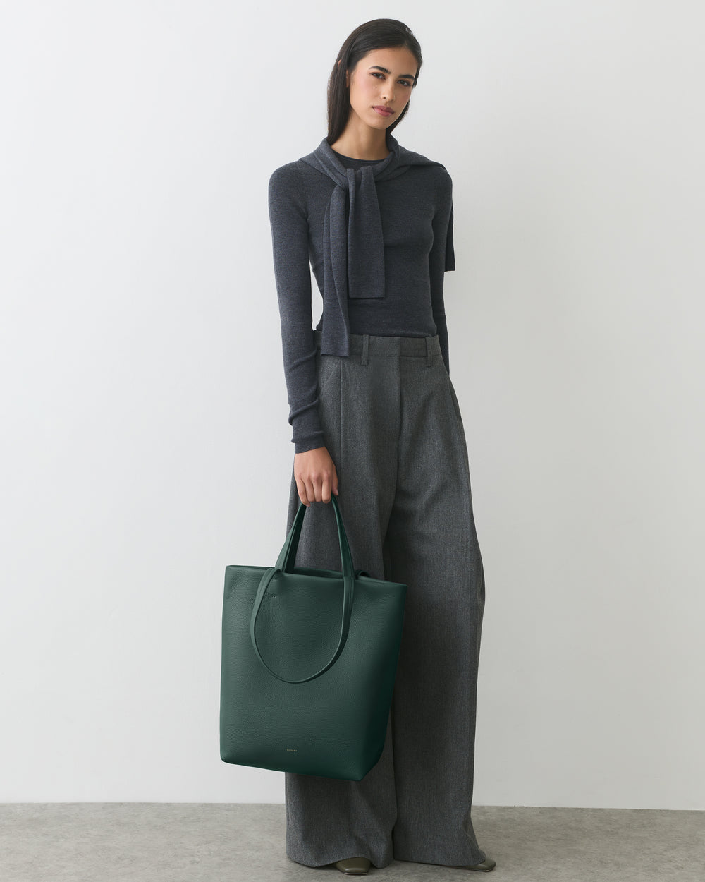 Person wearing sweater and pants holding a large tote bag.
