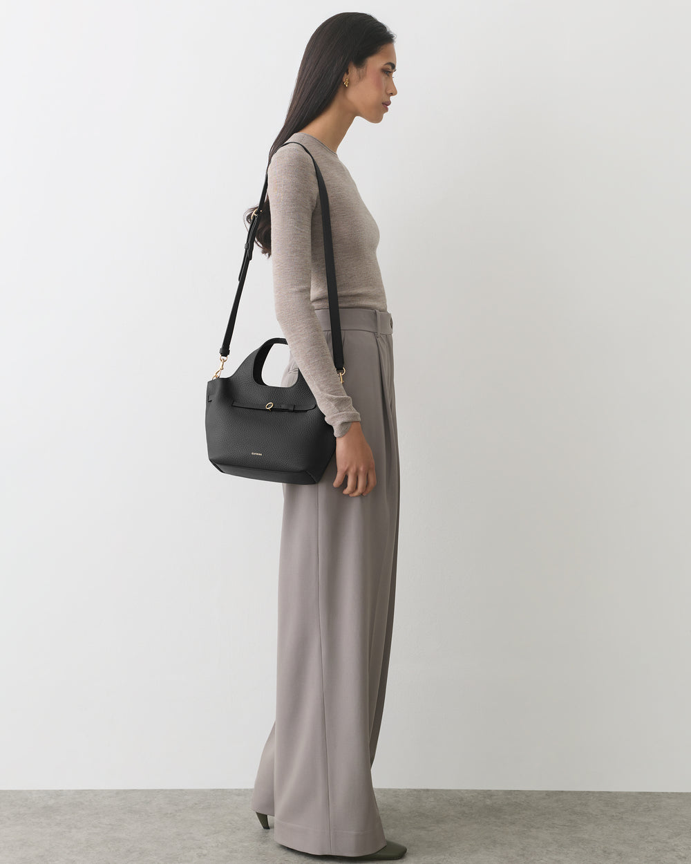 Woman in long-sleeve top and wide-leg pants carrying a shoulder bag.
