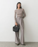 Person in long-sleeve top and wide-leg pants holding a small handbag.