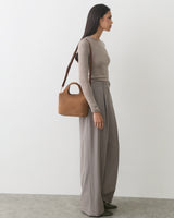 Person standing with handbag wearing long-sleeve top and wide-leg pants