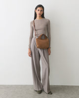 Person standing with a small shoulder bag and wearing long pants.