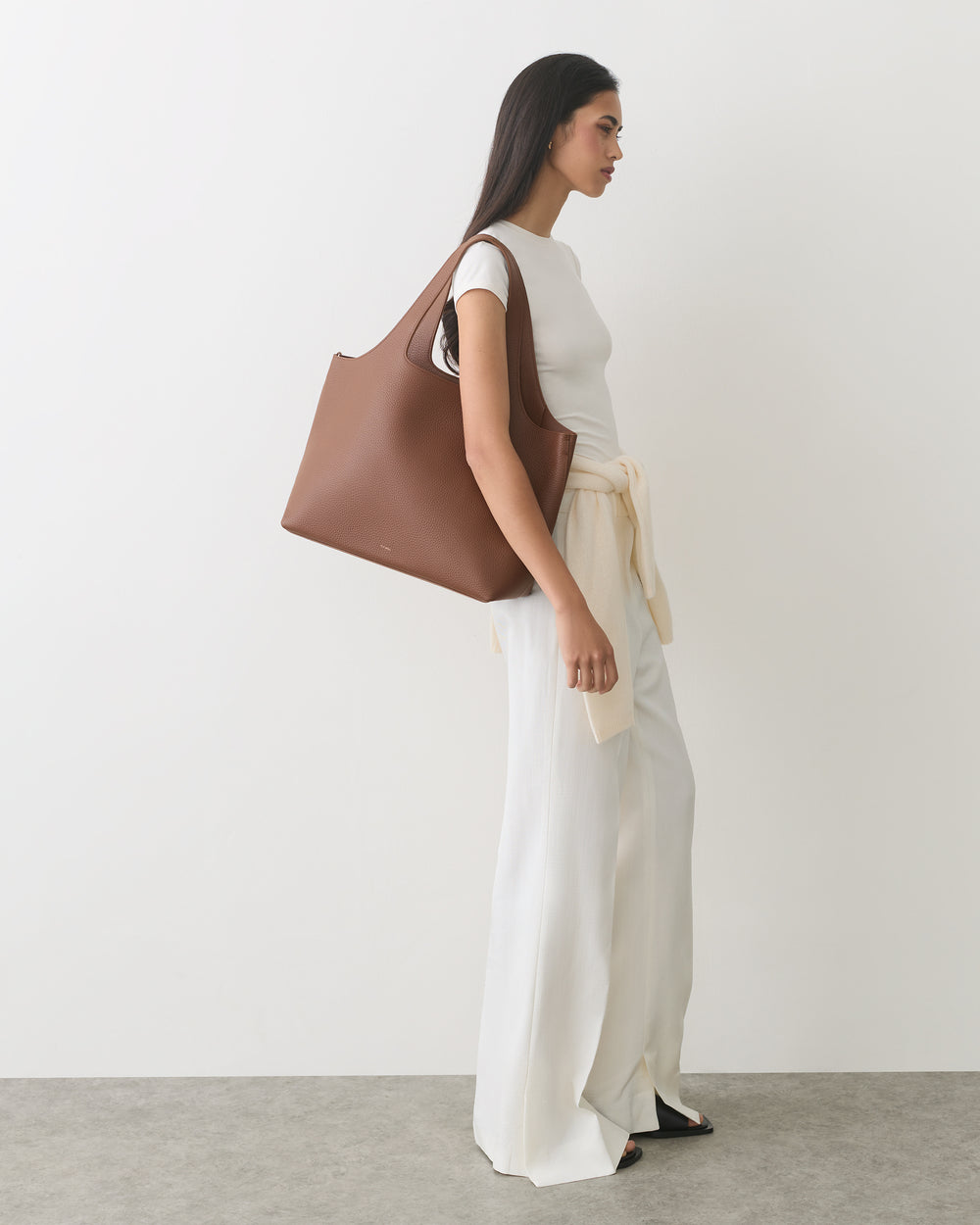 Person standing with large shoulder bag and wearing long pants and a short-sleeve top