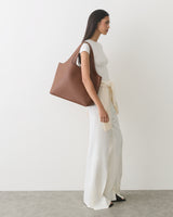 Person standing with large shoulder bag and wearing long pants and a short-sleeve top