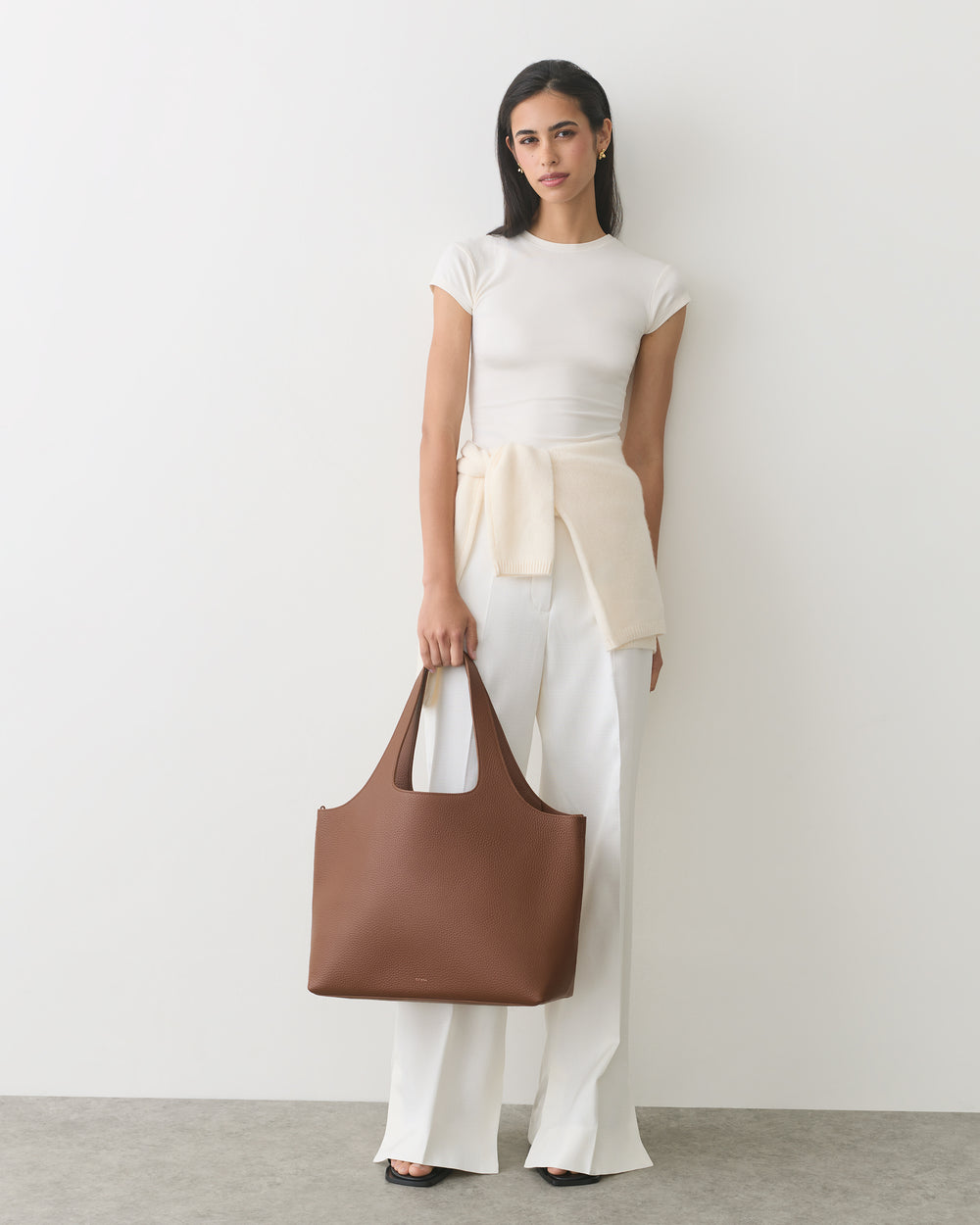 Person in white outfit holding a large handbag.