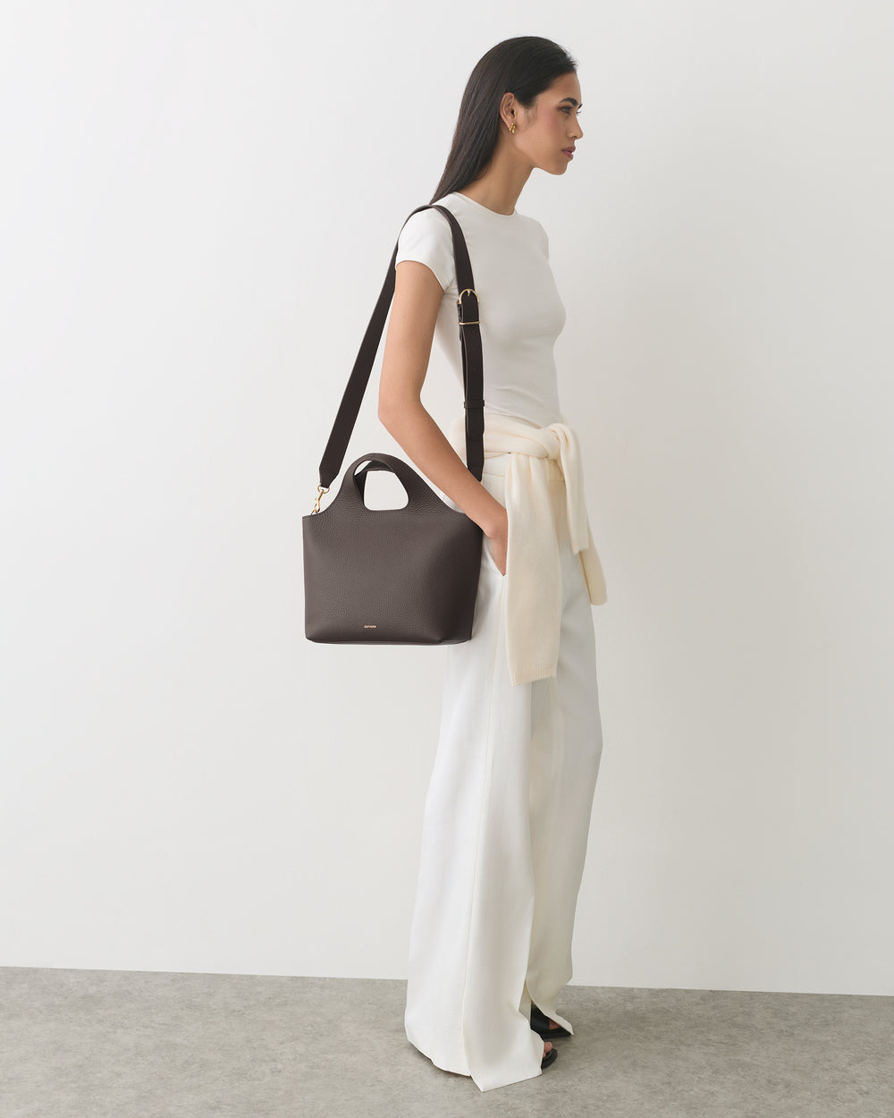 Person in white outfit carrying a handbag, with a sweater tied at the waist.