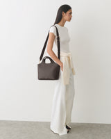 Person in white outfit carrying a handbag, with a sweater tied at the waist.