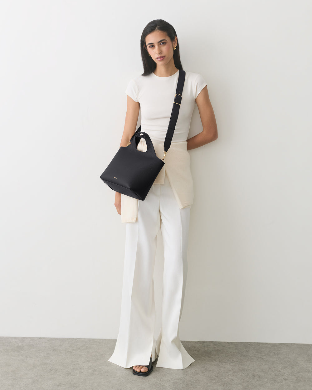 A person standing with a shoulder bag, wearing a short-sleeve shirt and wide-leg pants.