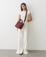 Person in a top and wide trousers holding a handbag with a strap over shoulder.