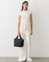 Person in a shirt and pants holding a handbag with a sweater around the waist