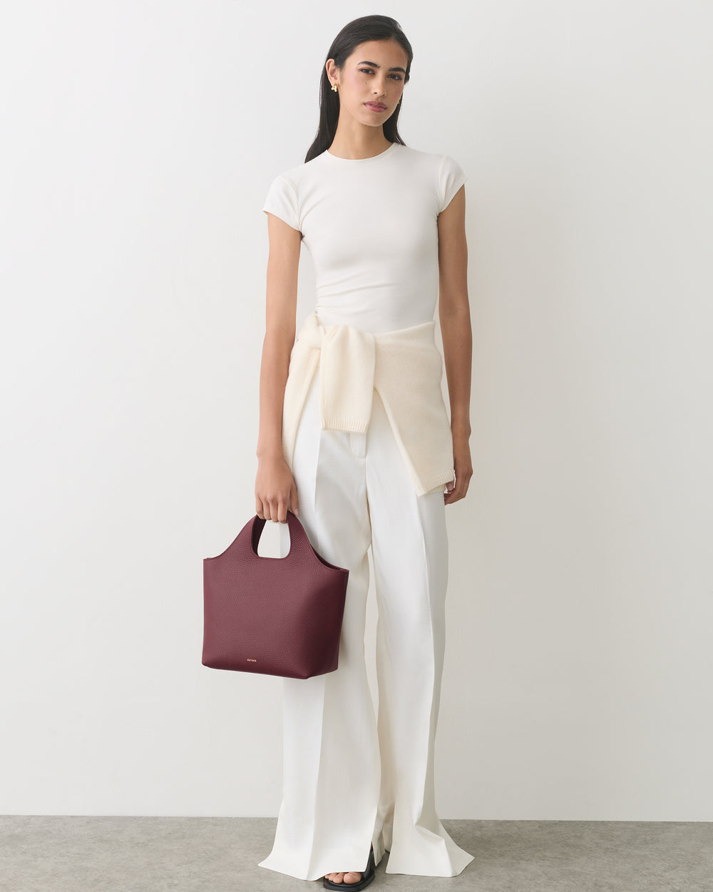 Person in a short-sleeve top and wide-leg pants holding a handbag.
