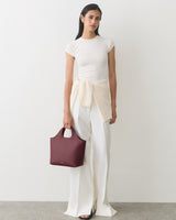 Person in a short-sleeve top and wide-leg pants holding a handbag.