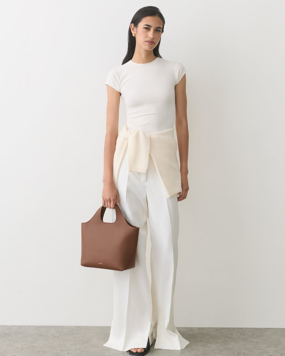 Person wearing outfit with wide pants and top, holding a handbag.