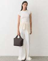 Person wearing a shirt and wide-leg pants, holding a handbag, with a sweater tied around waist.