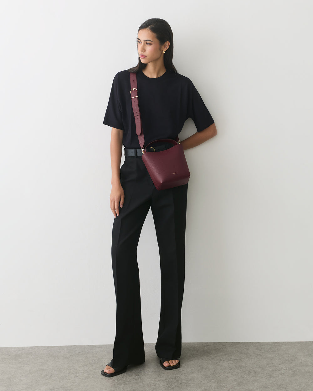 Person standing holding a shoulder bag, wearing a short-sleeve shirt and pants.