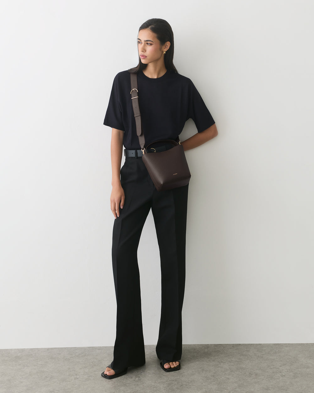 Person standing with shoulder bag, wearing a t-shirt and trousers.