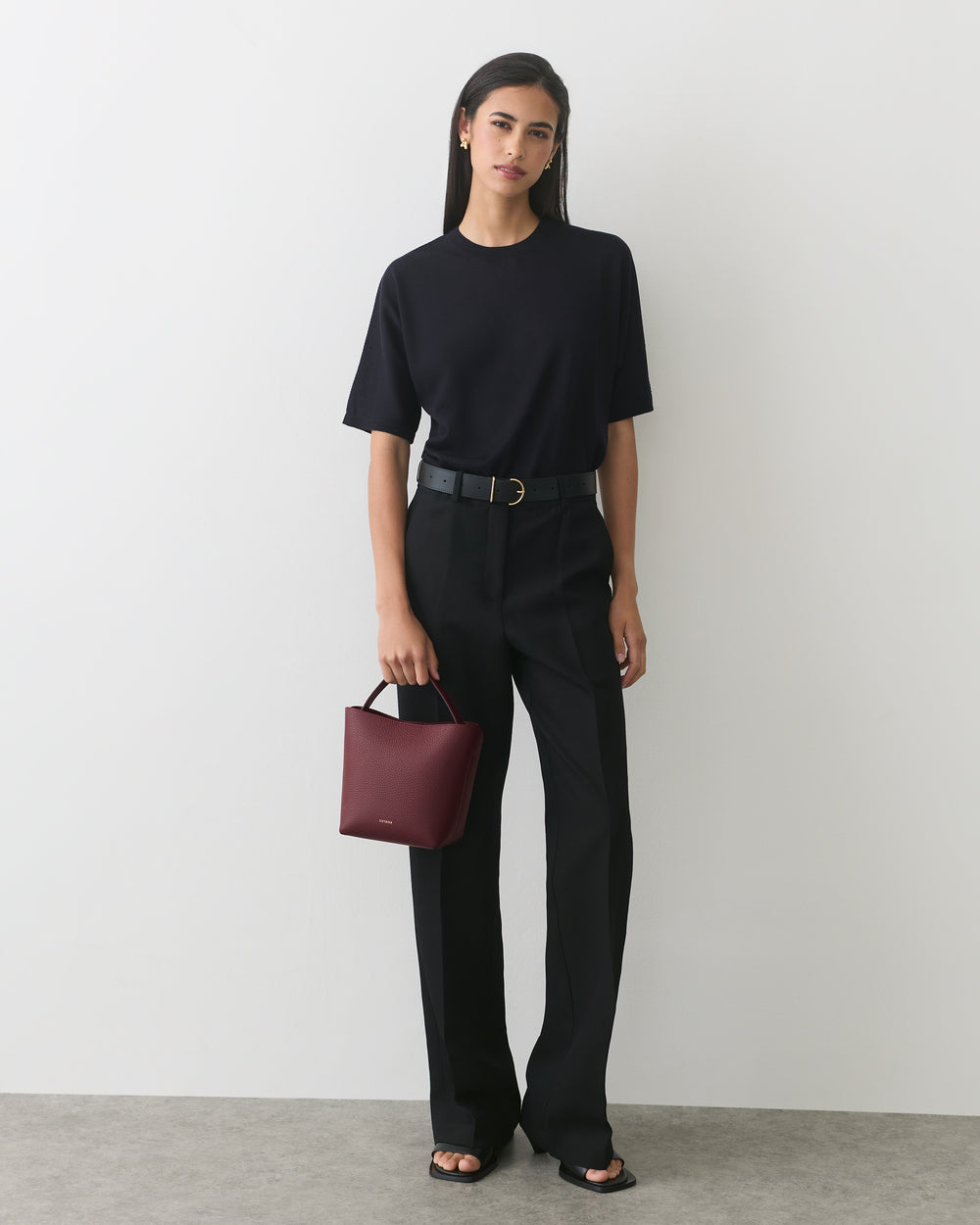 Person in casual outfit with short-sleeve top and long pants holds a small handbag