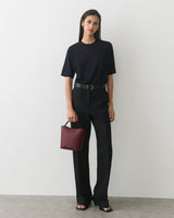 Person in casual outfit with short-sleeve top and long pants holds a small handbag