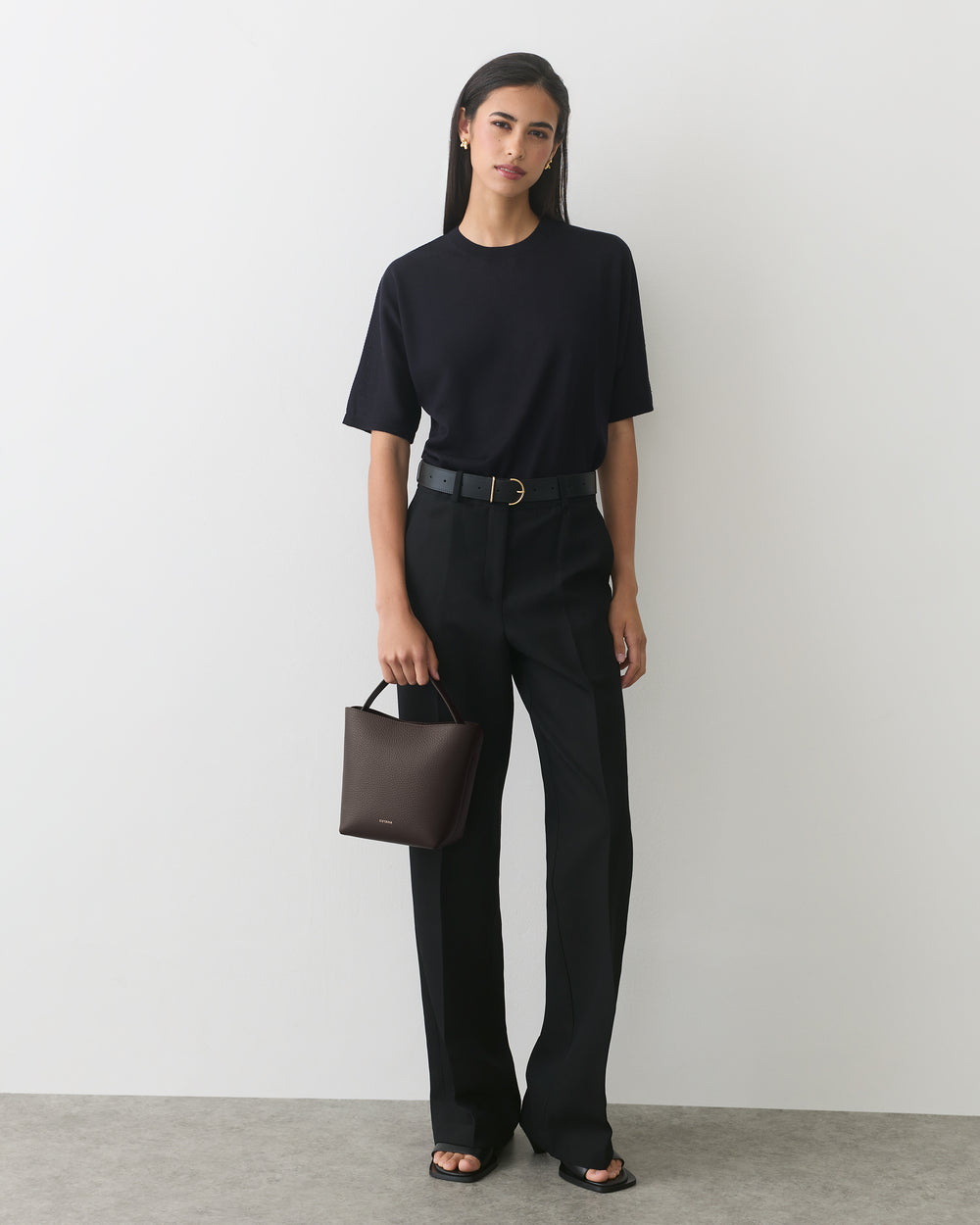 Person standing, wearing a t-shirt and pants, holding a small handbag.