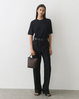 Person standing, wearing a t-shirt and pants, holding a small handbag.