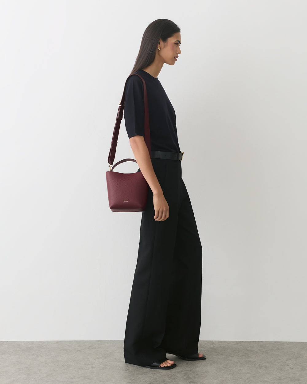 Person standing wearing wide-leg pants and holding a small handbag on the shoulder.