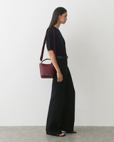 Person standing wearing wide-leg pants and holding a small handbag on the shoulder.