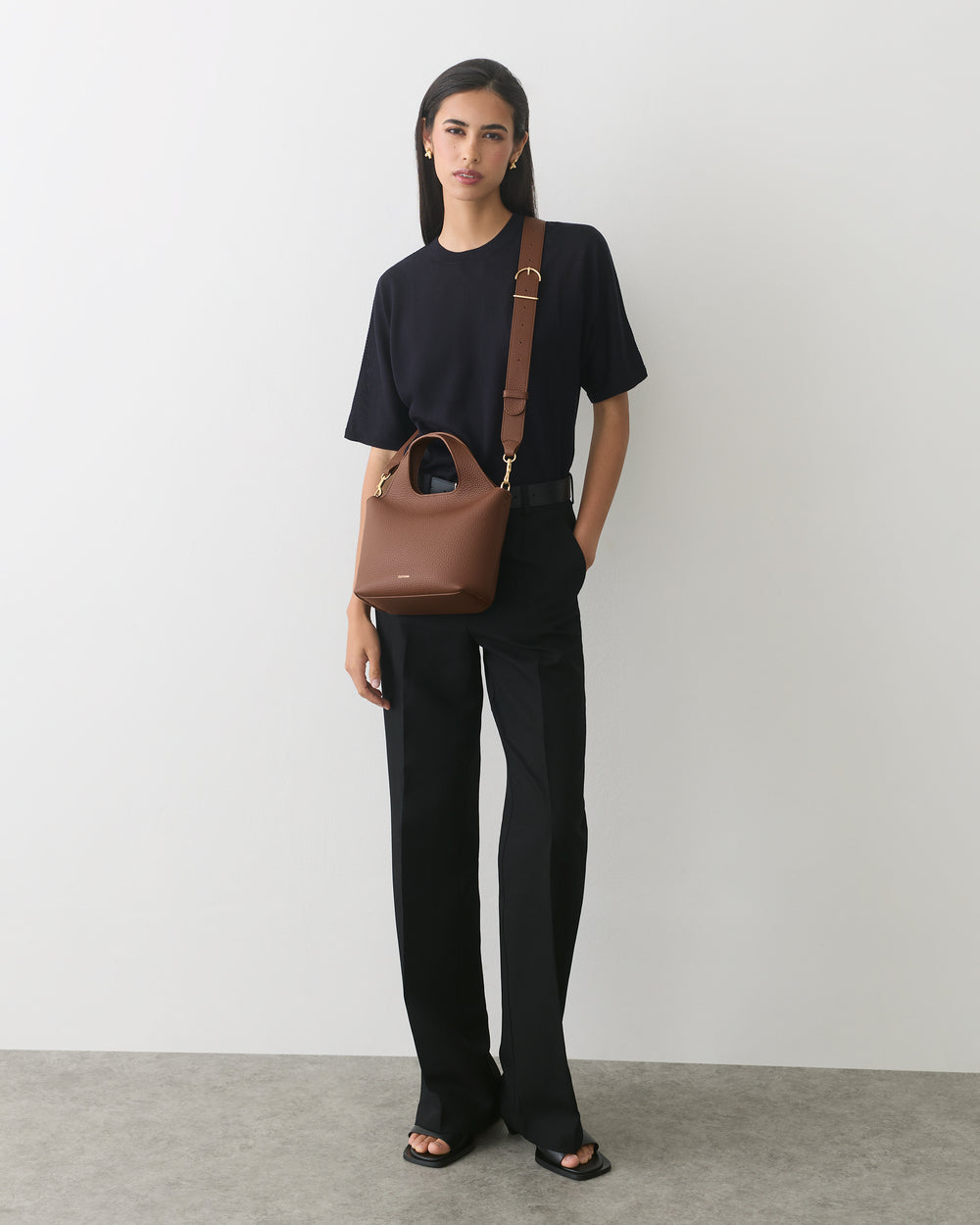 Person standing with a crossbody bag and wearing a short-sleeve shirt and long pants.