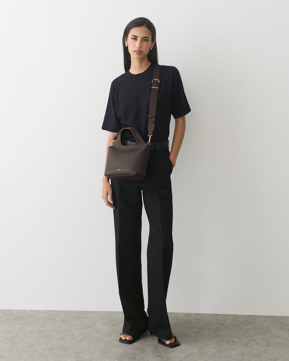 Person in a T-shirt and pants holding a handbag over the shoulder.