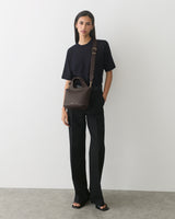 Person in a T-shirt and pants holding a handbag over the shoulder.