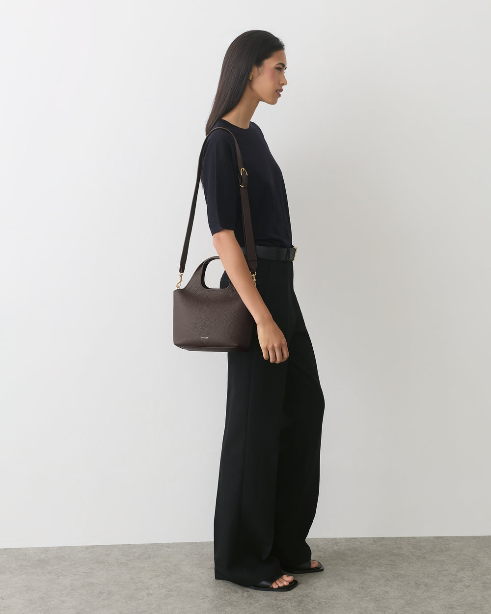 Person standing, wearing a short sleeve top and wide-leg pants, carrying a handbag.