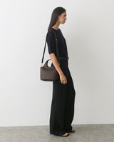 Person standing, wearing a short sleeve top and wide-leg pants, carrying a handbag.
