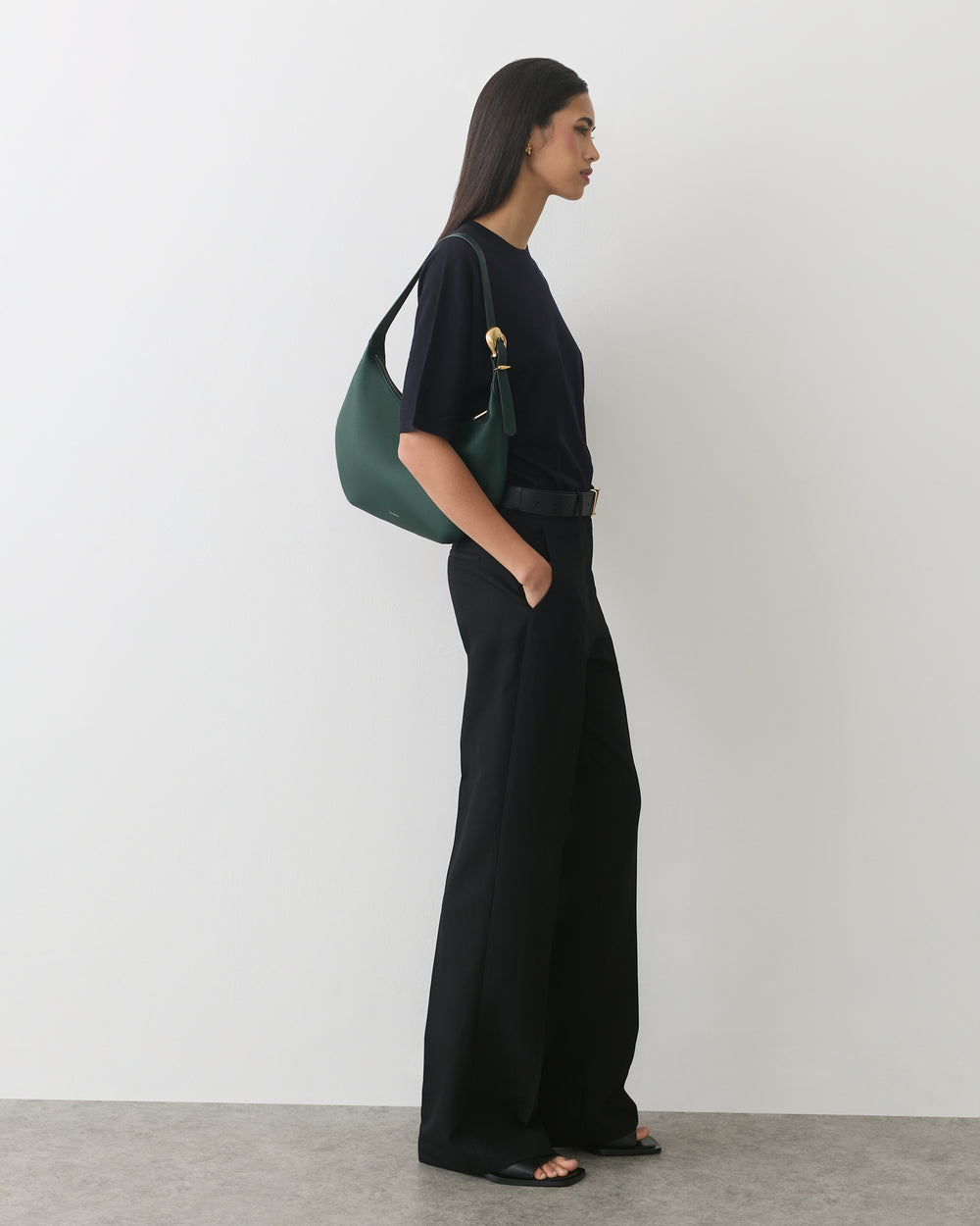 Person standing in profile with handbag on shoulder, wearing wide-leg pants and a short-sleeve top.