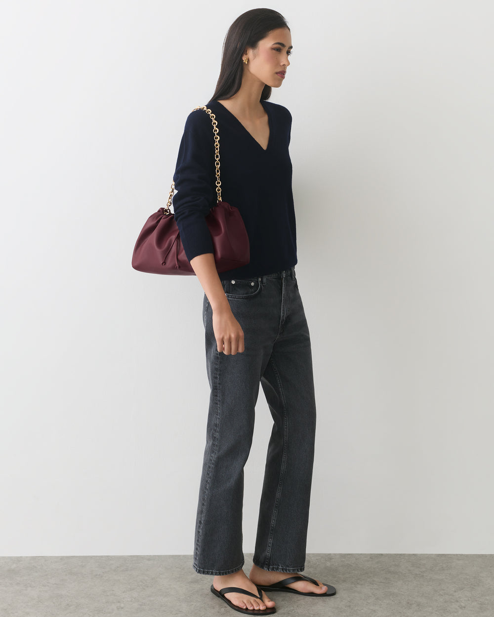 Person wearing a V-neck sweater, jeans, sandals, carrying a shoulder bag with a chain strap.