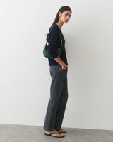Person standing in profile, wearing a long-sleeve top and jeans, carrying a shoulder bag.