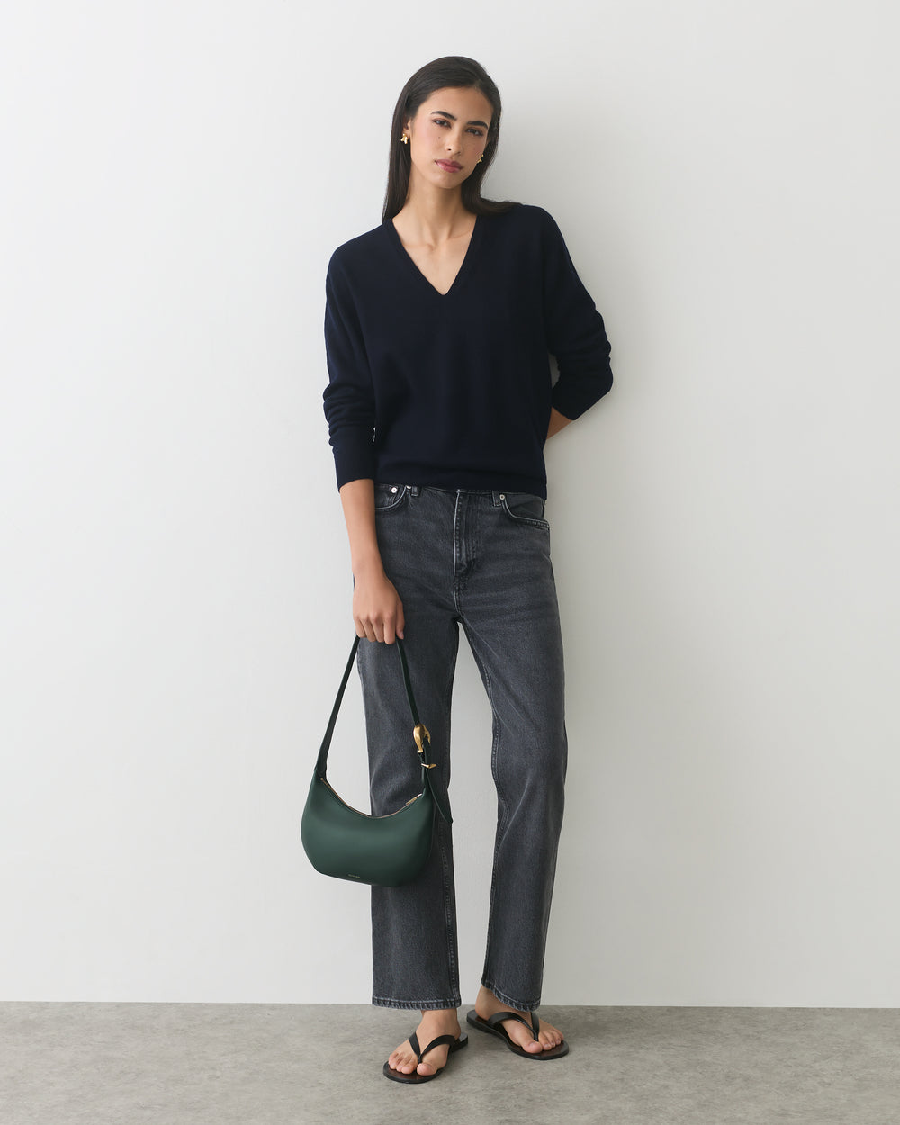 Person wearing a sweater and jeans, holding a handbag, standing against a plain background.