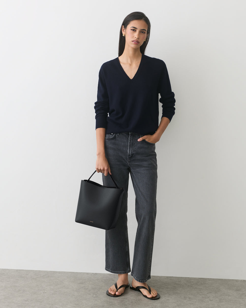 Person in sweater and jeans holding handbag, wearing sandals.