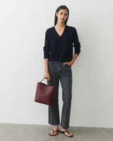 Person wearing a sweater and jeans holding a handbag, standing against a plain background.