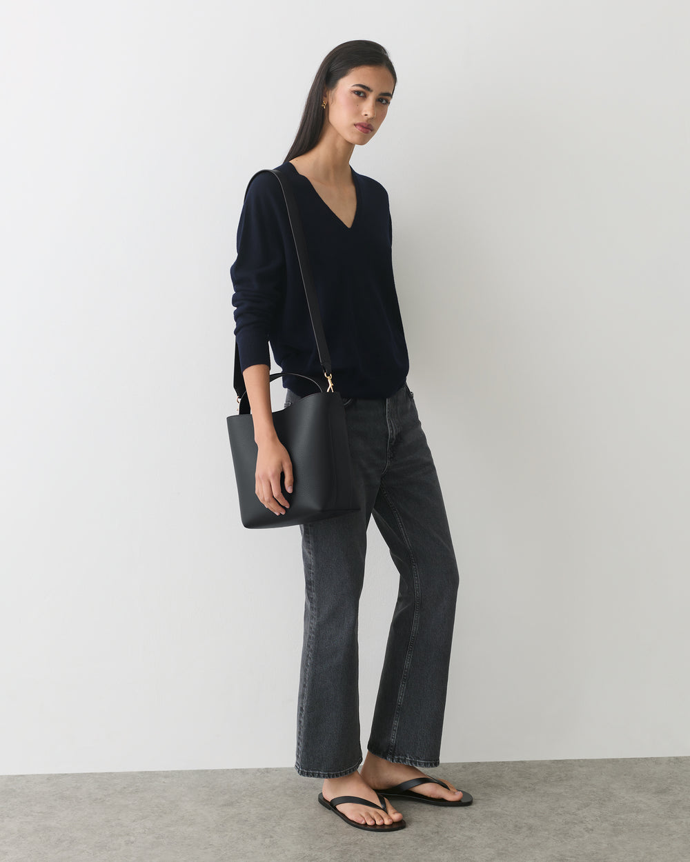 Person wearing a long sleeve top and jeans, holding a shoulder bag, wearing sandals.