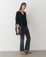 Person wearing a long sleeve top and jeans, holding a shoulder bag, wearing sandals.