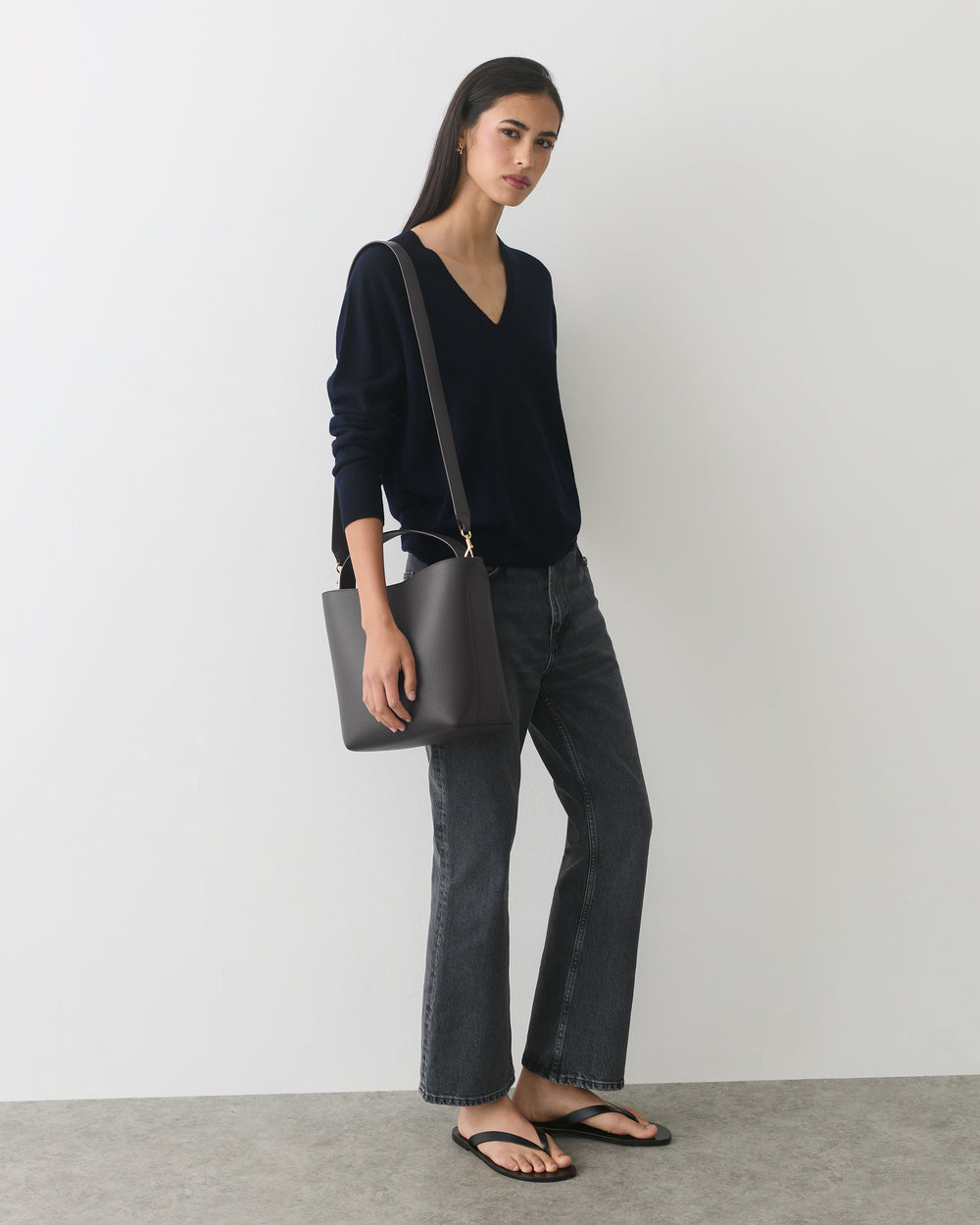 Person in a sweater and jeans holding a shoulder bag standing indoors.