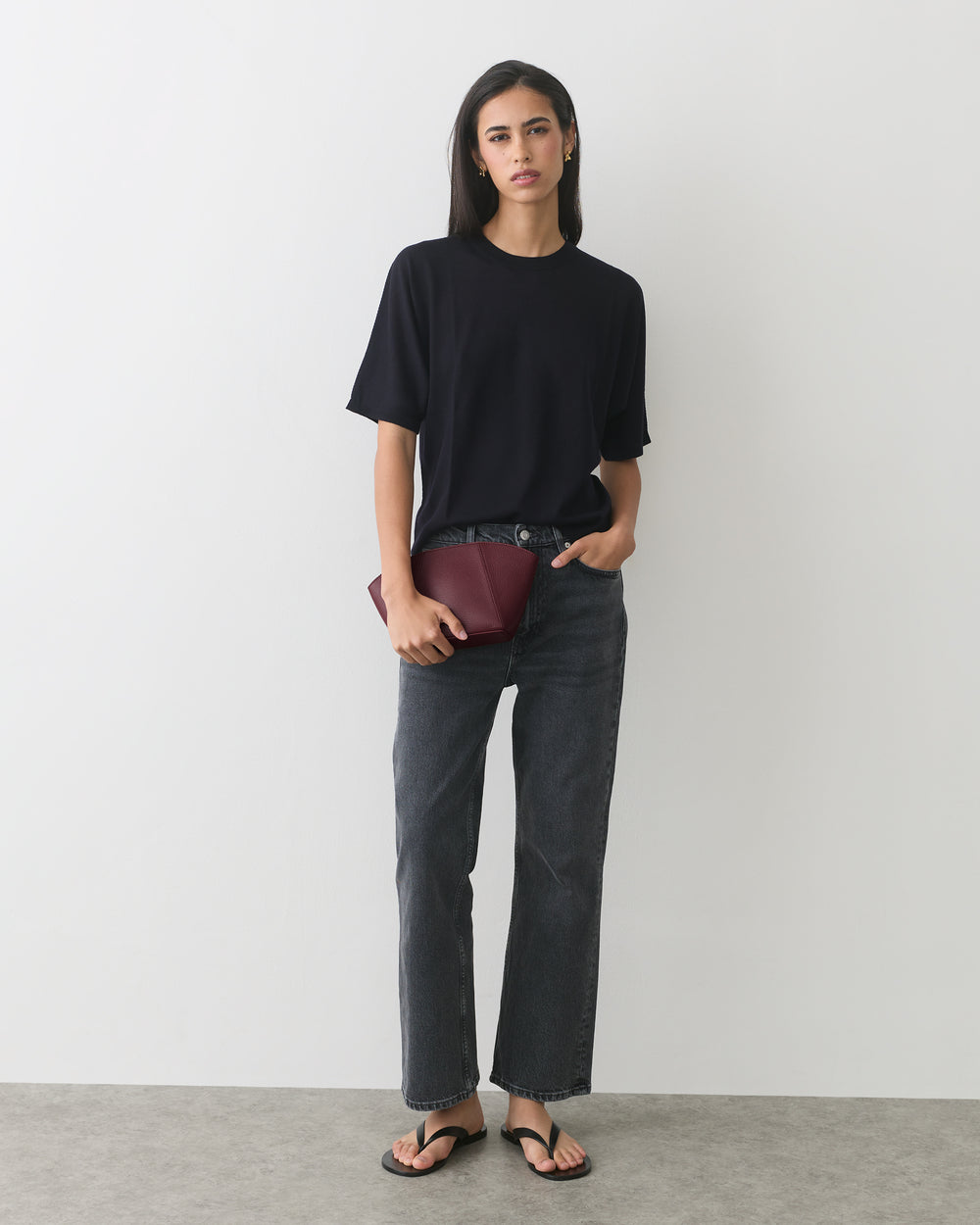 Person wearing a T-shirt, jeans, sandals, holding a clutch bag.