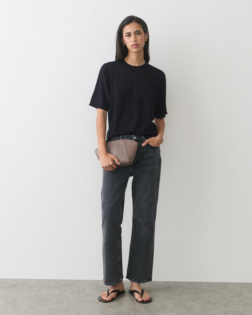 Person in a t-shirt and jeans holding a clutch, wearing sandals.