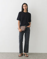 Person in a t-shirt and jeans holding a clutch, wearing sandals.