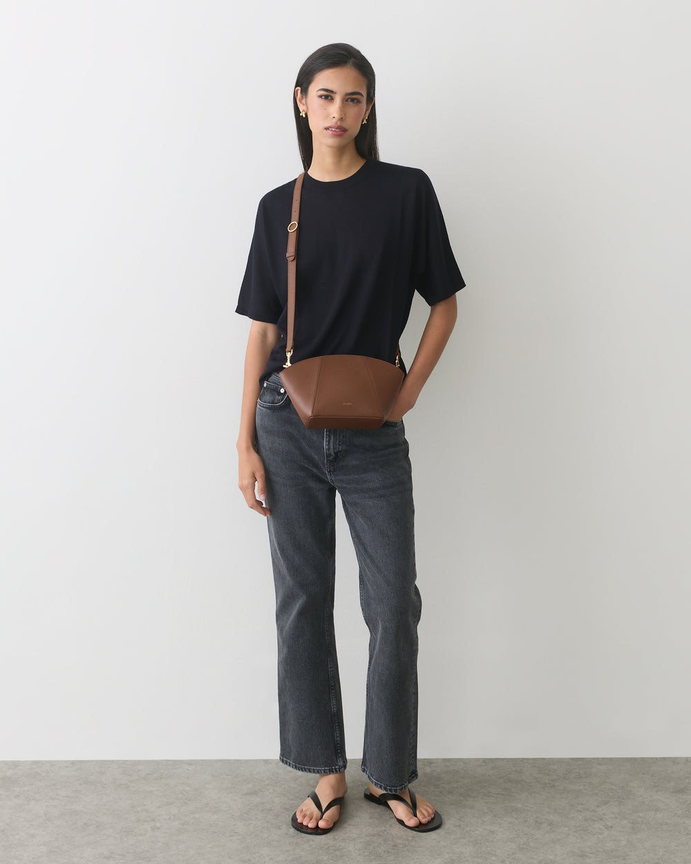 Person standing with a belt bag, wearing a t-shirt, jeans, and sandals.