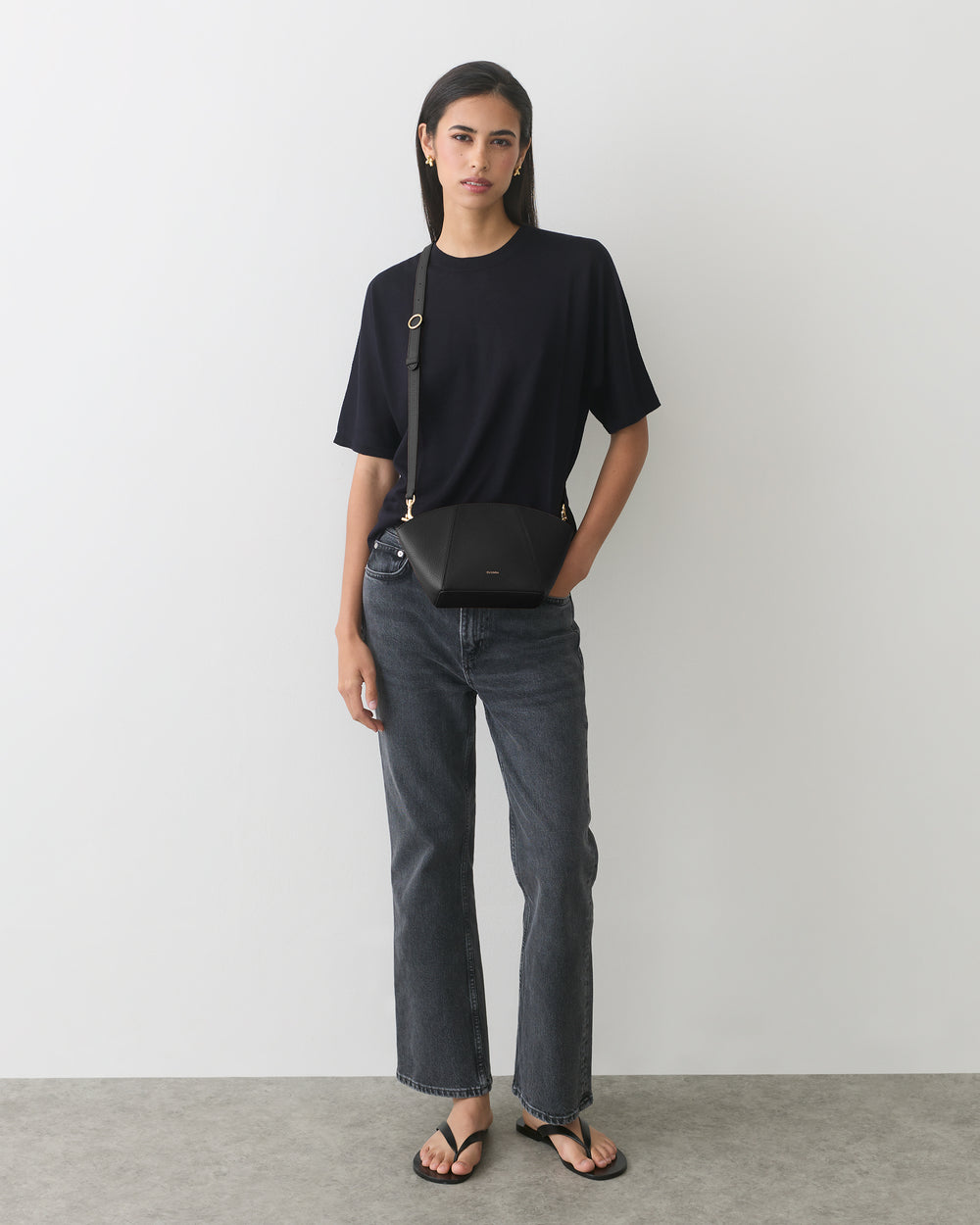 Person wearing t-shirt and jeans with a belt bag and sandals.