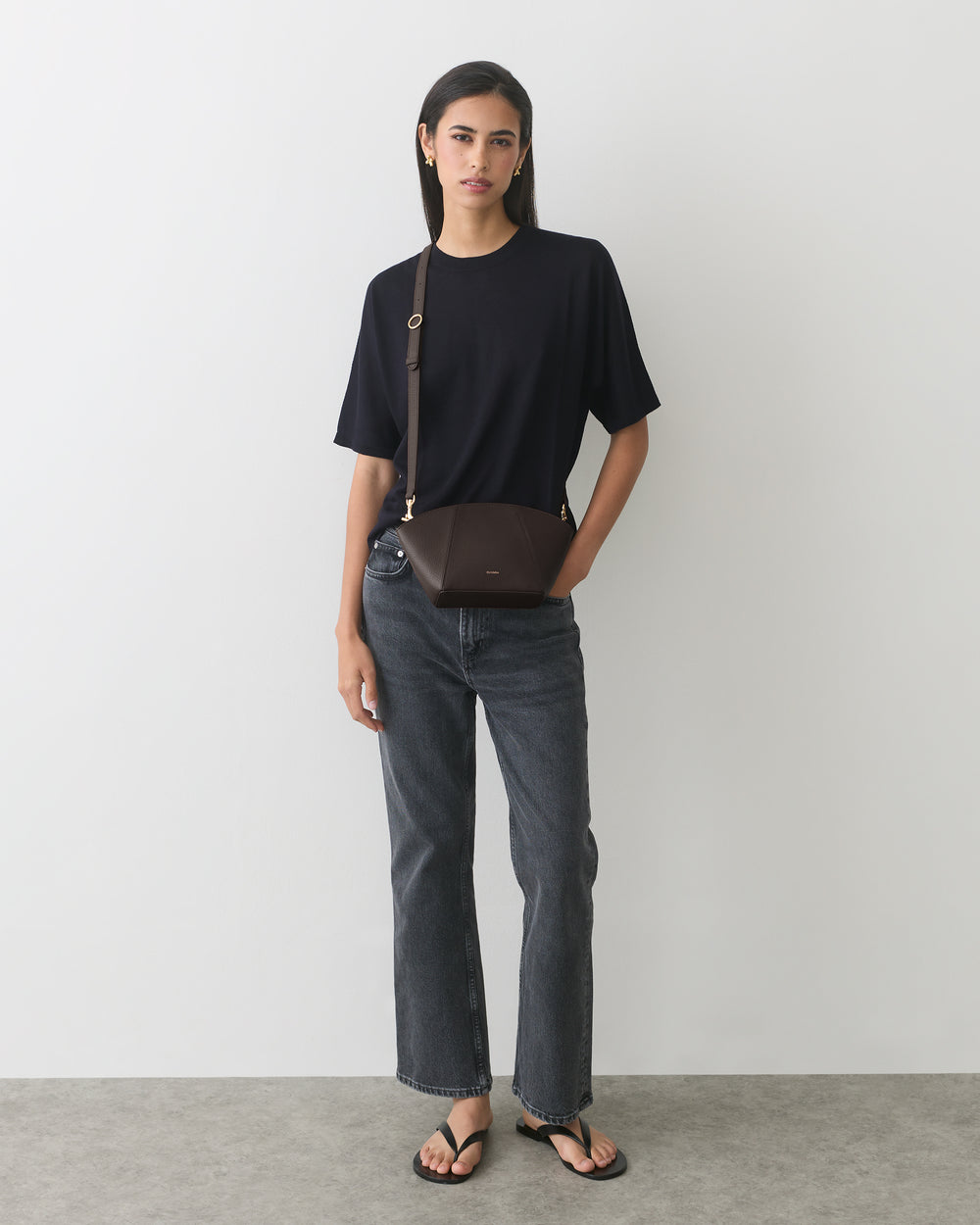 Person wearing a t-shirt, jeans, sandals, and a belt bag, standing against a plain background.
