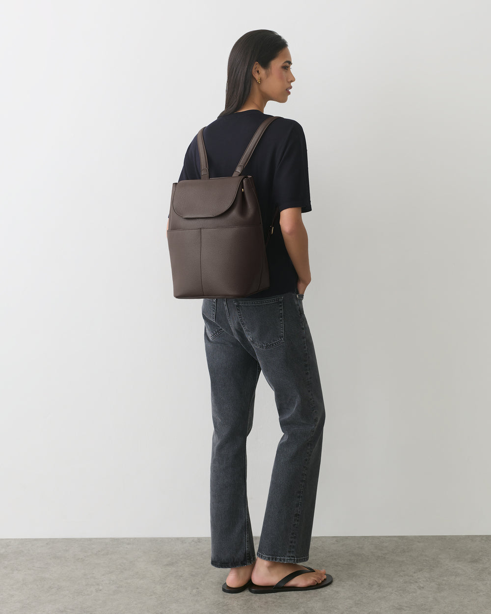 Person with backpack facing sideways, wearing jeans and sandals.