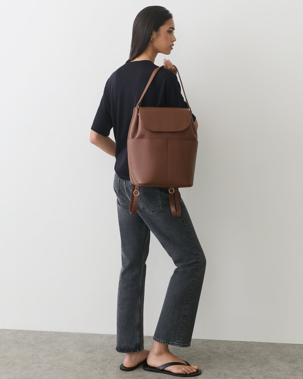 Person standing, holding travel bag over shoulder, wearing casual outfit with sandals.