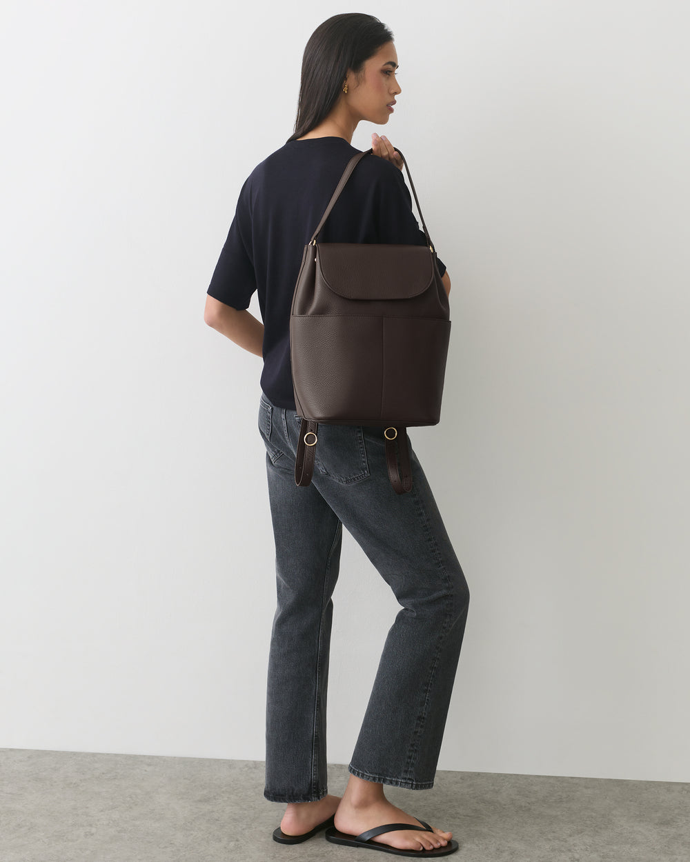 Person with backpack wearing casual outfit and sandals in a minimalistic setting.