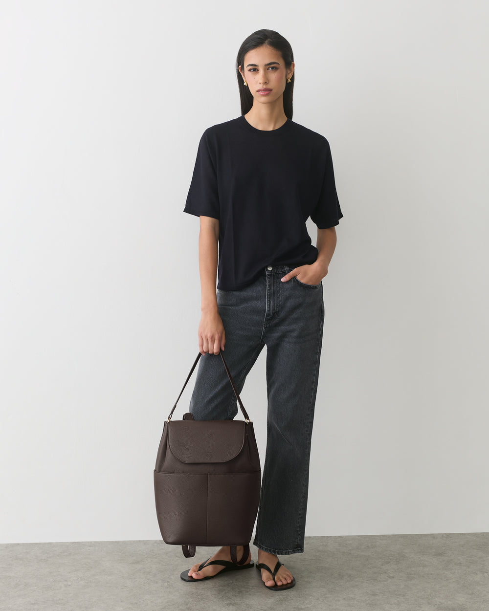 Person in casual outfit holding a large bag, standing against a plain background.