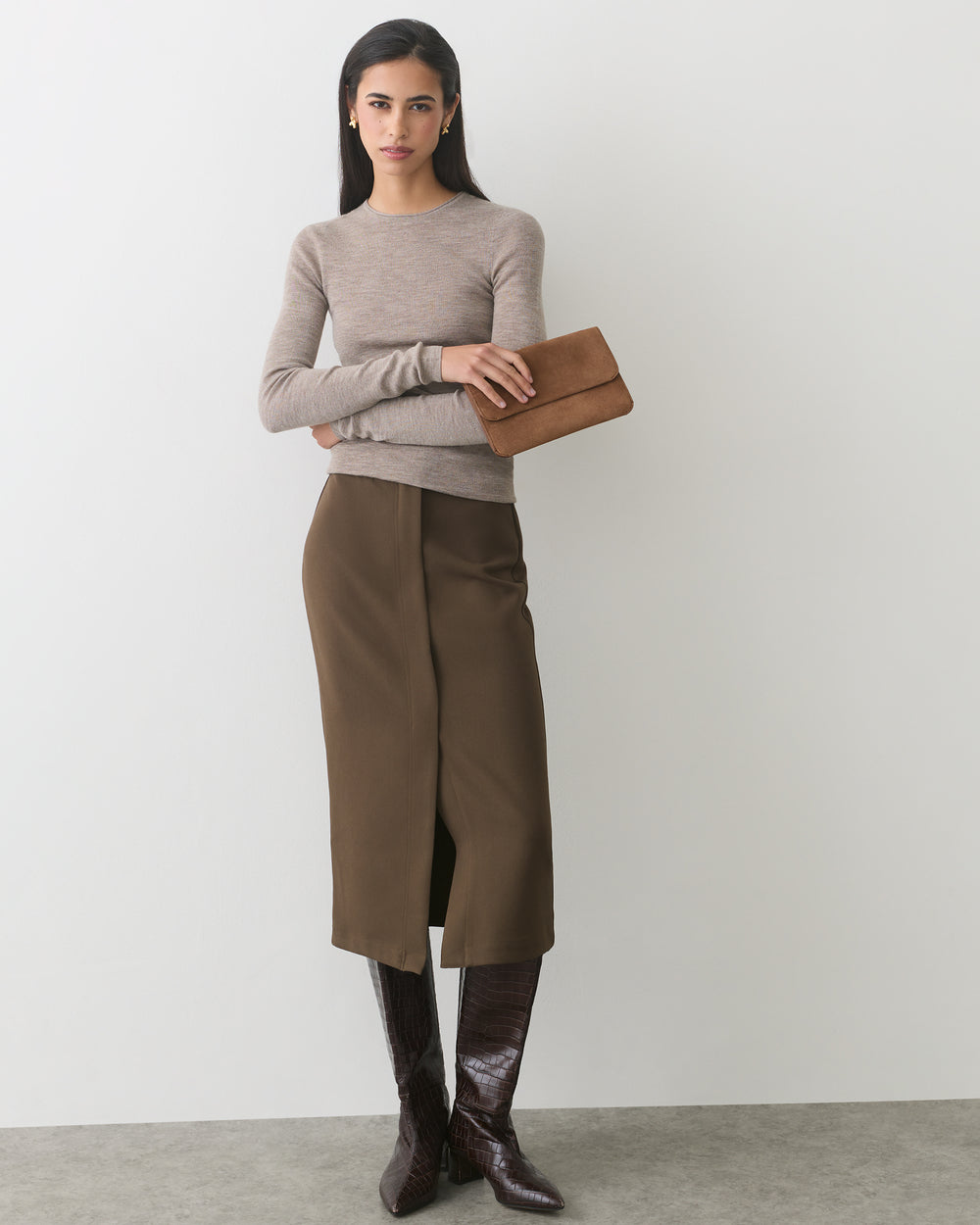 Person in long skirt and boots holding a clutch.